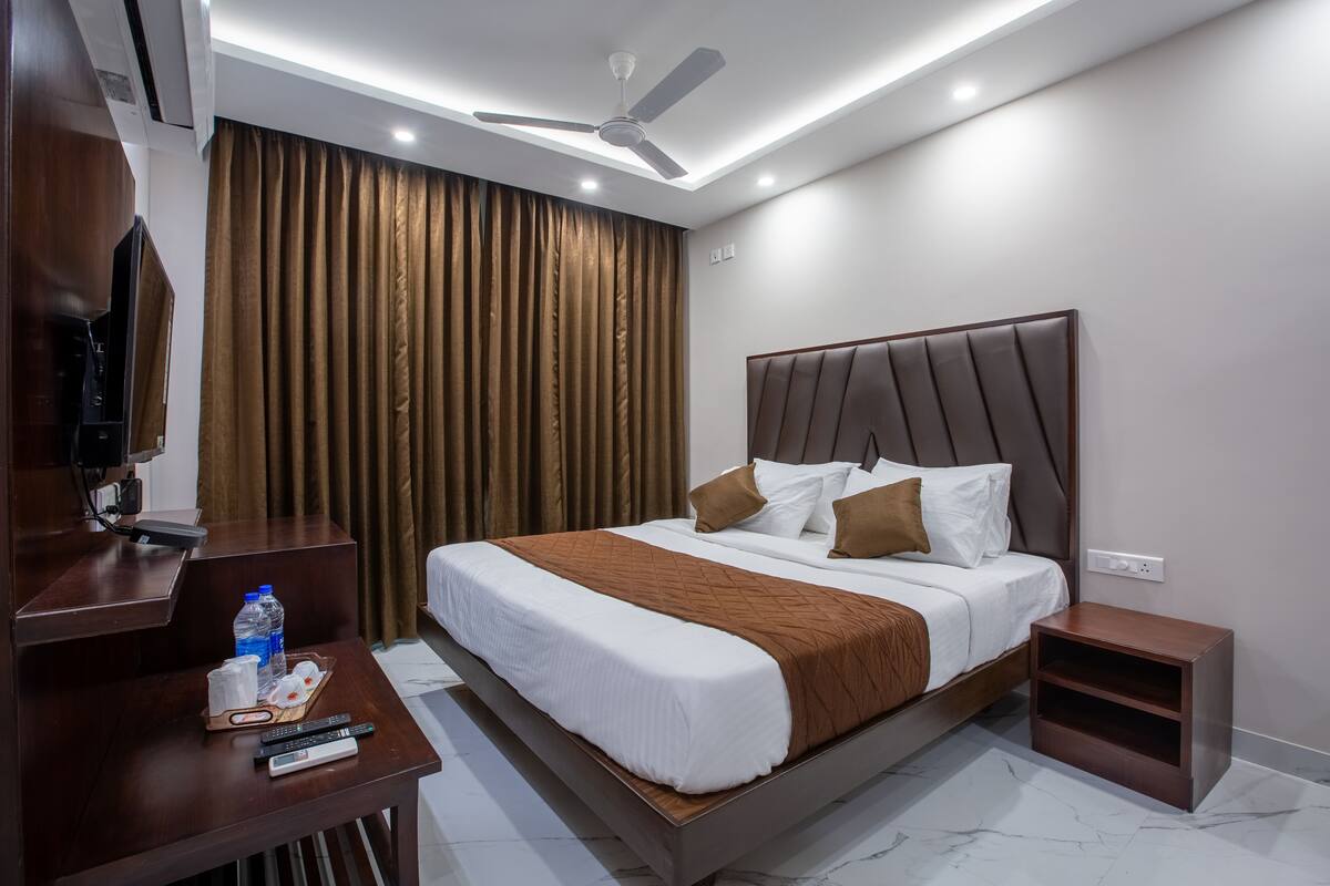 A modern hotel room with a large bed, a desk with a TV, and a ceiling fan.