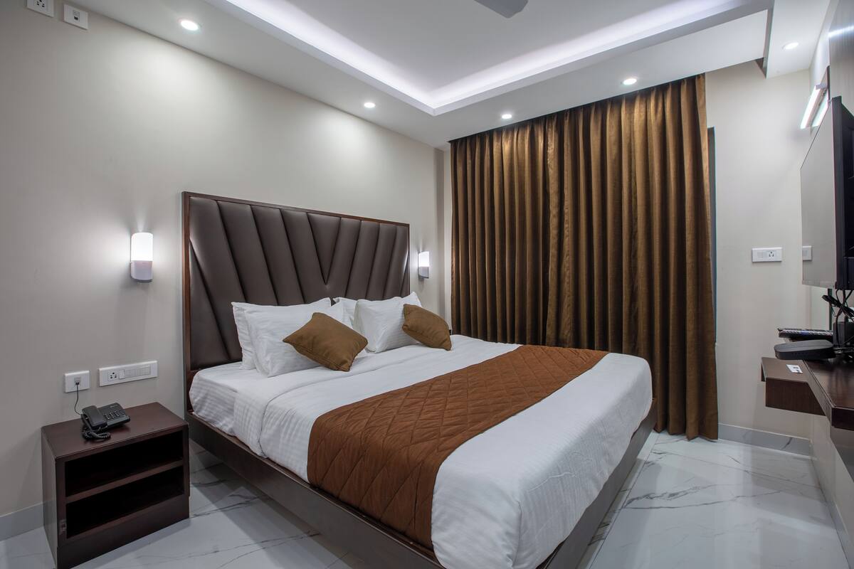 A modern hotel room with a large bed, a bedside table with a phone, and a flat-screen TV on a stand.