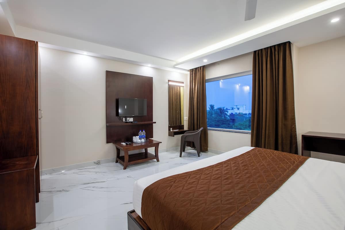 A hotel room with a large bed, a TV, a desk, and a window with a city view.