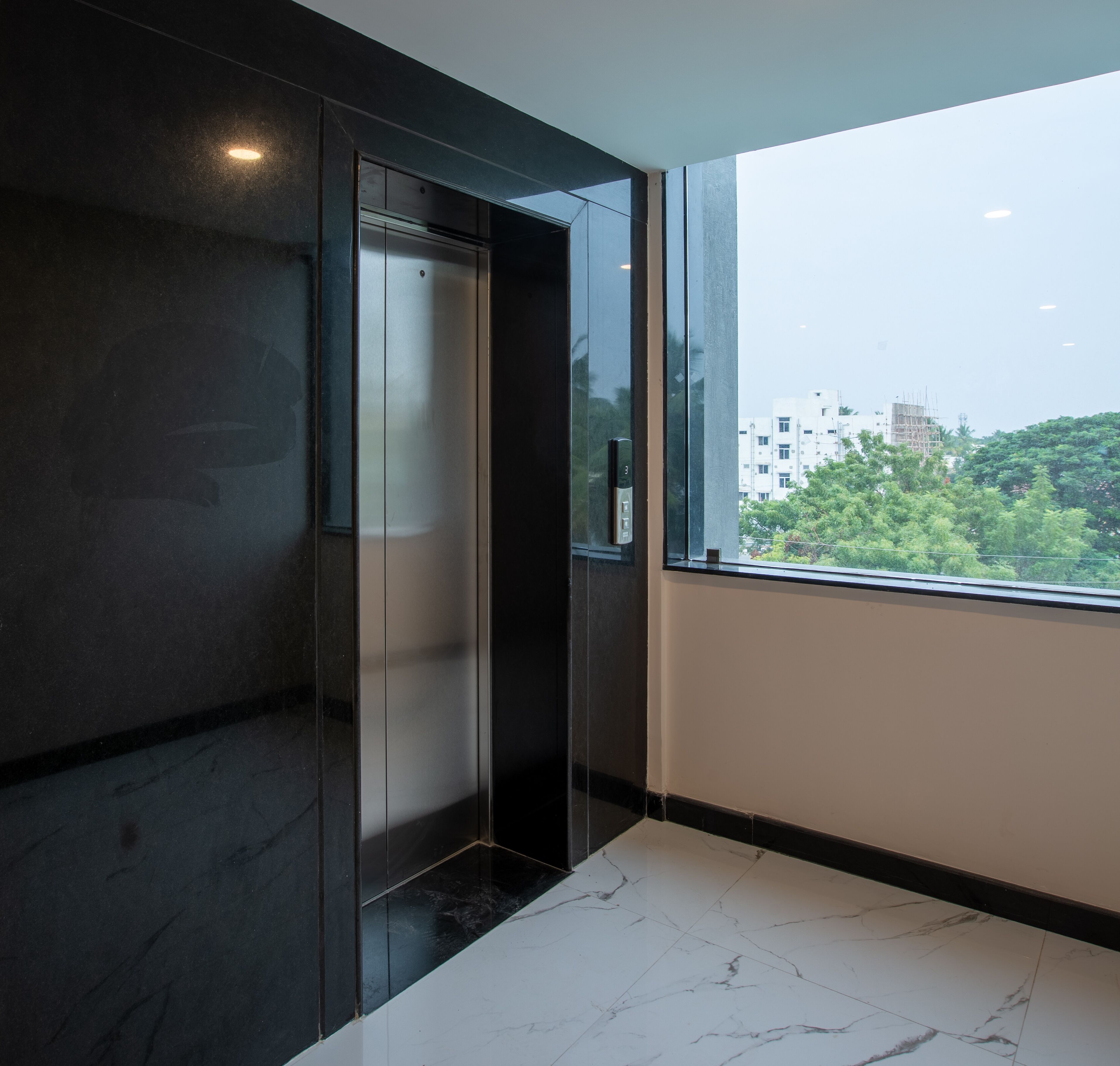 A modern elevator with a metallic finish, a marble-tiled floor, and a view of a cityscape through a large window.