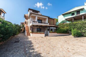 A two-story building with a stone-paved courtyard, a covered outdoor seating area, and a small garden. - Piazzetta Albatros 50m From The Beach (Loiri Porto San Paolo)