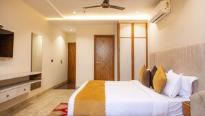 A modern hotel room with a large bed, a ceiling fan, an air conditioning unit, a wooden wardrobe, and a flat-screen TV mounted on the wall. - Hotel Eminence (Mohali)