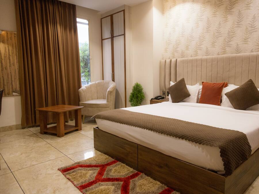 Un dormitorio con una cama grande, una mesita de noche, una pequeña mesa, una silla y una ventana con cortinas.