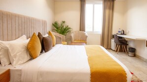 A hotel room with a large bed, a desk, a chair, and a potted plant. - Hotel Eminence (Mohali)