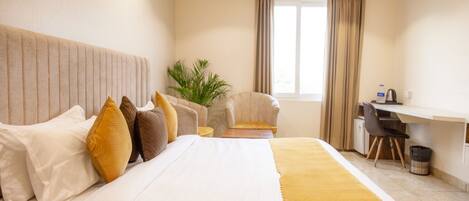 A hotel room with a large bed, a desk, a chair, and a potted plant.