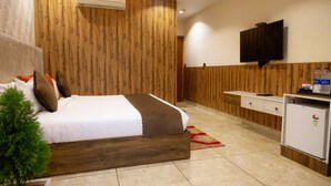 A bedroom with a bed, a small desk, a television, and an air conditioning unit. - Hotel Eminence (Mohali)