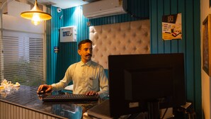 A hotel reception desk with a tufted headboard, a computer, and a sign instructing guests to submit their room keys. - Hotel Eminence (Mohali)