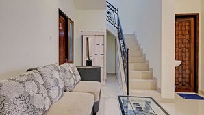 A living room with a sofa, a glass coffee table, a staircase, and a wooden door. - OYO Life 92935 Ayu Kost Eksklusif (Ngaglik)