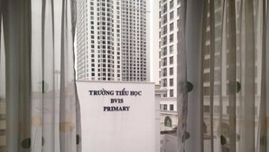 Letrero que dice 'TRƯỜNG TIẾU HỒC BVIS PRIMARY' con vista a edificios altos al fondo.