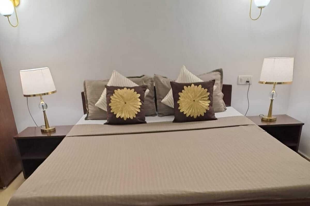 A neatly made bed with a beige bedspread and two decorative pillows with a sun-like design. There are two bedside lamps on wooden nightstands.