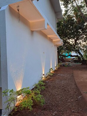 Um edifício branco com varanda coberta e área de jardim com plantas e uma mangueira.