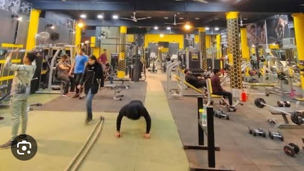 Une salle de sport équipée de divers appareils d’exercice, de ventilateurs au plafond et d’un éclairage lumineux.