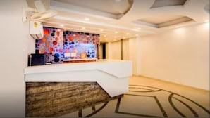 Un espace d’accueil doté d’un bureau blanc moderne, d’un mur orné d’une œuvre abstraite aux couleurs vives et d’un tapis à motifs.