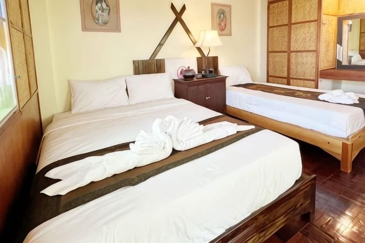 Een hotelkamer met twee bedden, een houten hoofdeinde, een nachtkastje met een lamp en een klein tafeltje met een vaas.