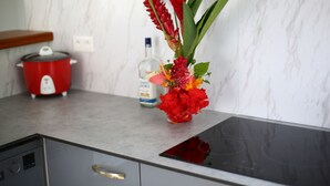 Une cuisine équipée d’une cuisinière moderne, avec une casserole rouge, une bouteille et un vase rempli de fleurs posés sur le comptoir.