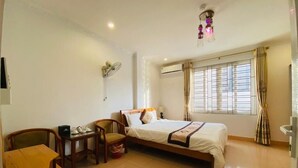 Habitación de hotel con cama, escritorio, silla, una mesita con tetera y ventana con cortinas.