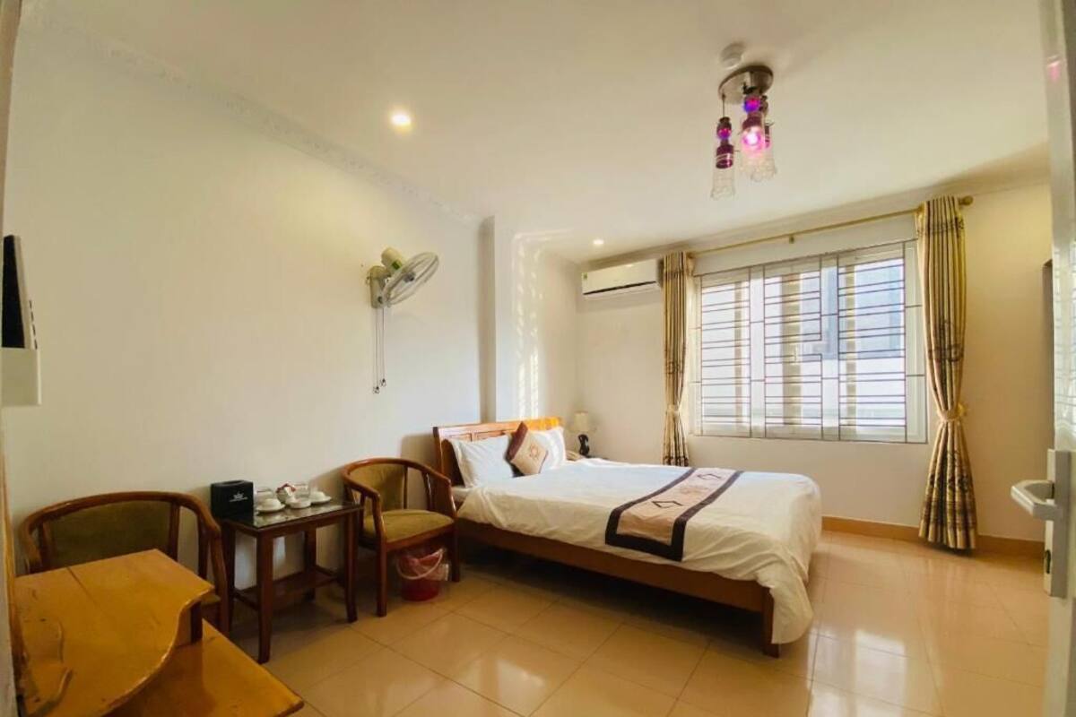 Habitación de hotel con cama, escritorio, silla, una mesita con tetera y ventana con cortinas.