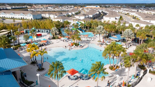 Ein Resort mit einem großen zentralen Pool, Palmen und verschiedenen Sitzbereichen im Freien.