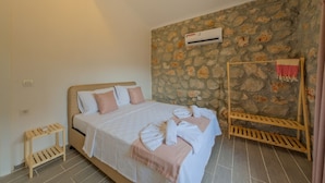 A bedroom with a stone wall, a bed with pillows, a wooden bedside table, and an air conditioning unit.