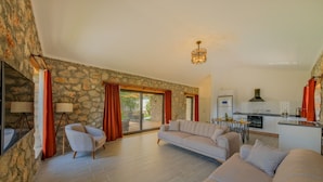 A spacious living area with a stone wall, a sofa, a chair, and a kitchen in the background.