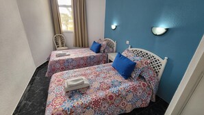 A room with two beds, each with patterned bedding and a blue pillow. There is a chair and a small table. The walls are painted blue, and there are two wall-mounted lights. - Guayero 2 (Los Cristianos)