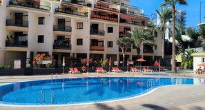 A swimming pool with sun loungers and umbrellas, surrounded by a multi-story building with balconies. - Guayero 2 (Los Cristianos)