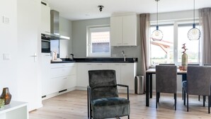A modern kitchen with white cabinets, a black countertop, and a dining area with a table and chairs. - Holiday Home near Scherpenisse Beach (Scherpenisse)