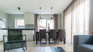 A modern kitchen with white cabinets, a dining area with a table and chairs, and a living area with a sofa. - Holiday Home near Scherpenisse Beach (Scherpenisse)