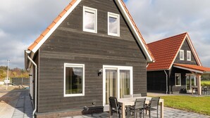 A modern two-story house with a dark wooden exterior, a red-tiled roof, and a patio with a table and chairs. - Holiday Home near Scherpenisse Beach (Scherpenisse)