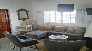 Un salon avec un canapé gris, une table basse ronde, un fauteuil gris, une porte en bois et un grand miroir au mur.