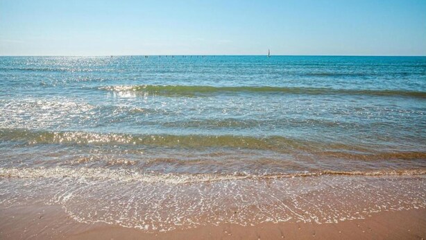 Une plage avec une eau d’un bleu limpide et un phare situé au loin.