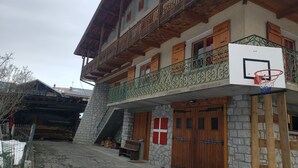 Ein zweistöckiges Gebäude mit Balkon, Stein-Fassade, Holztüren und einem Basketballkorb.