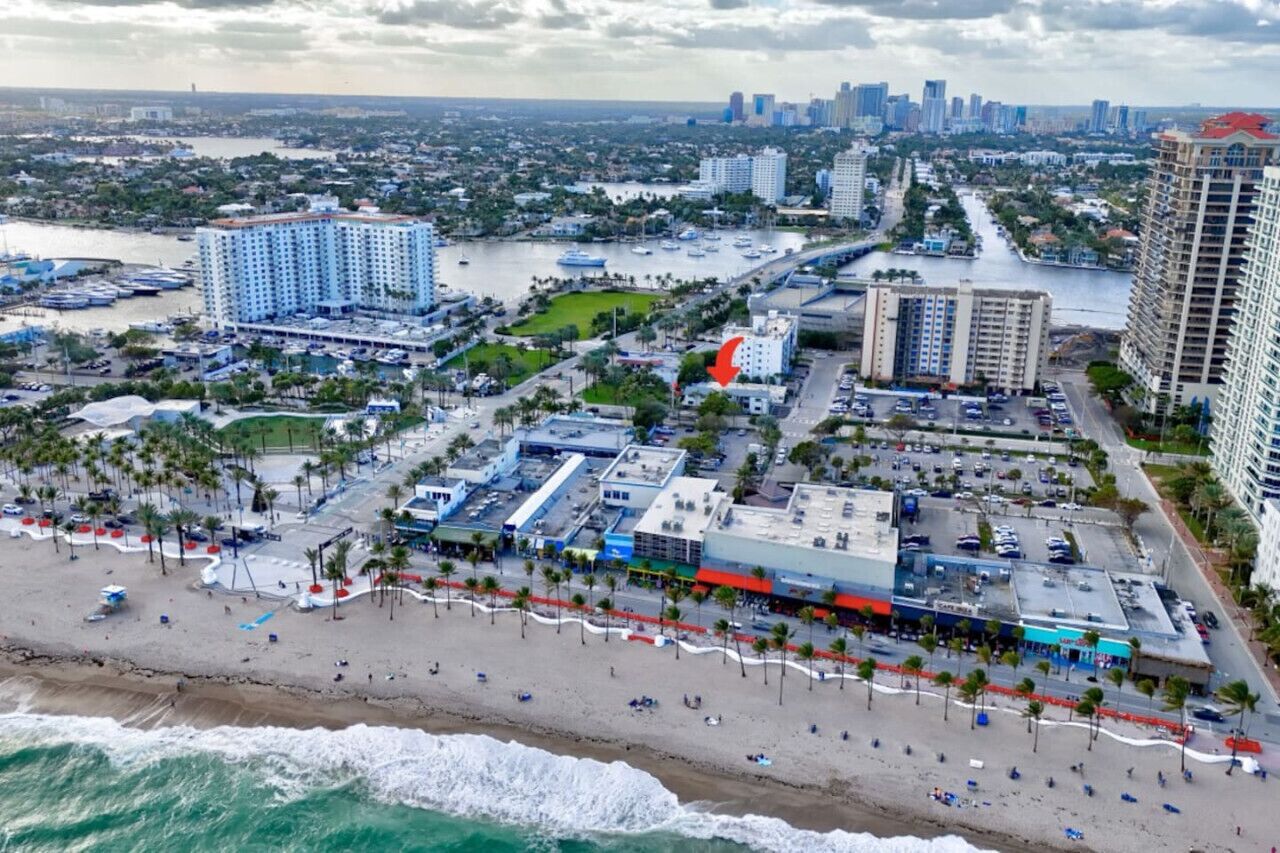 A coastal cityscape with a beachfront hotel, a marina, and high-rise buildings in the background.