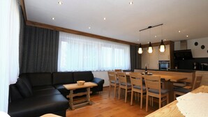 Un salon moderne avec un canapé noir, une table à manger en bois et des chaises. Il y a également un coin cuisine avec une cuisinière et des placards.