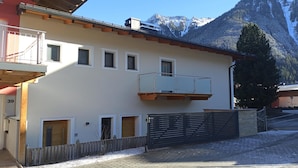 Un bâtiment à deux étages doté d’un balcon, d’une clôture en bois et ayant une chaîne de montagnes en arrière-plan.