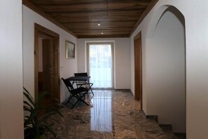 Um corredor com teto de madeira, uma mesa dobrável preta e cadeiras, levando a uma porta com janela.