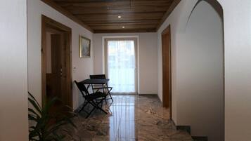 A hallway with a wooden ceiling, a black folding table, and chairs, leading to a door with a window.