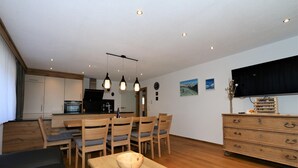 A modern kitchen with wooden cabinets, a dining area with a table and chairs, a TV on the wall, and a wooden dresser. - Beautiful holiday flat in Krimml near waterfalls (Krimml)