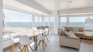 Een ruime kamer met een grote tafel en stoelen, een bank en uitzicht op het strand.