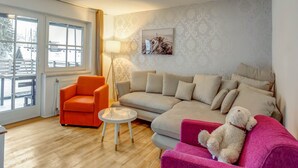 Ett vardagsrum med en soffa, en orange fåtölj, ett litet bord och ett stort fönster.