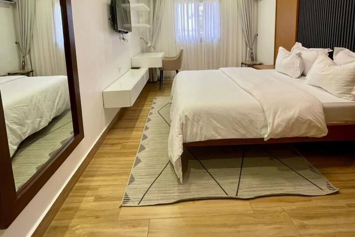 A modern hotel room with a large bed, a desk, a chair, and a TV on the wall.