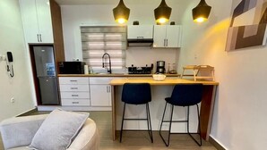 A modern kitchen with a central island, two bar stools, and pendant lighting. - Swanky  Apartments (Douala)