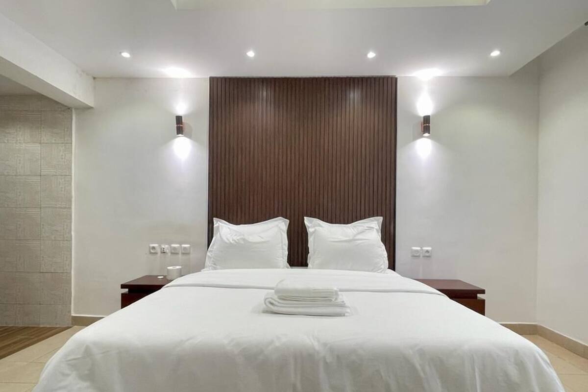 A modern hotel room with a large bed, two bedside tables, and a wooden headboard.