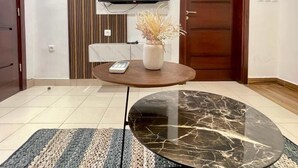 A modern living room with a flat-screen TV mounted on the wall, a round coffee table with a marble top, and a patterned rug on the floor. - Swanky  Apartments (Douala)
