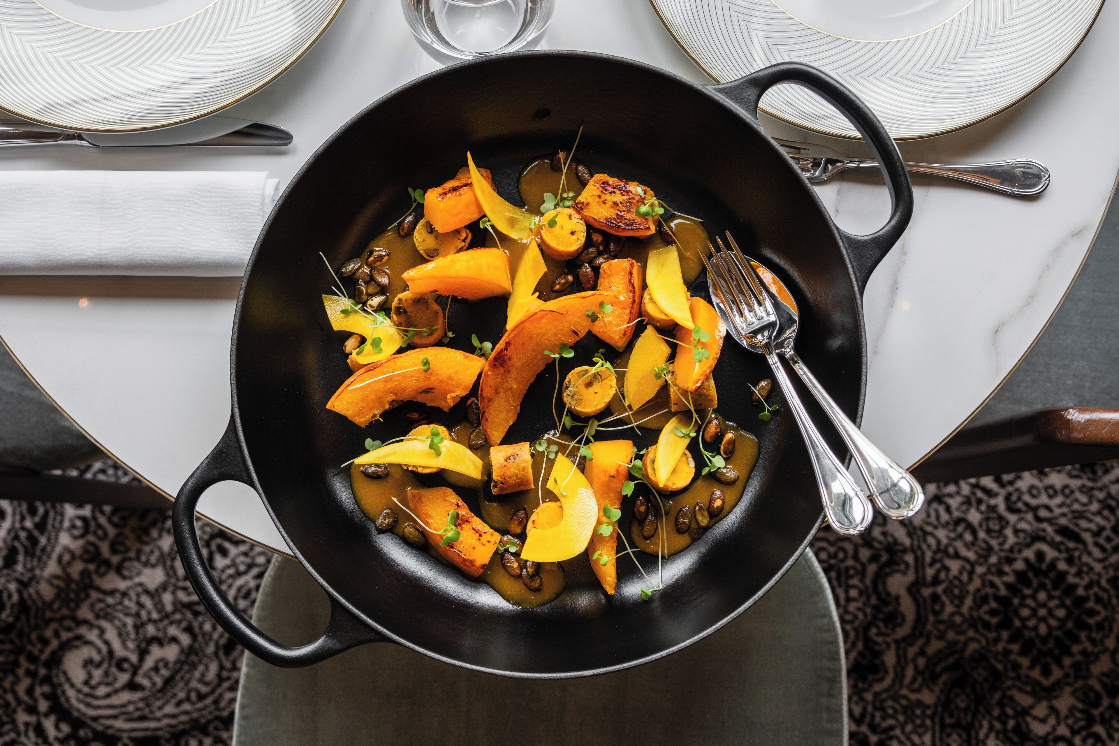A pan of roasted vegetables with a fork and spoon beside it.