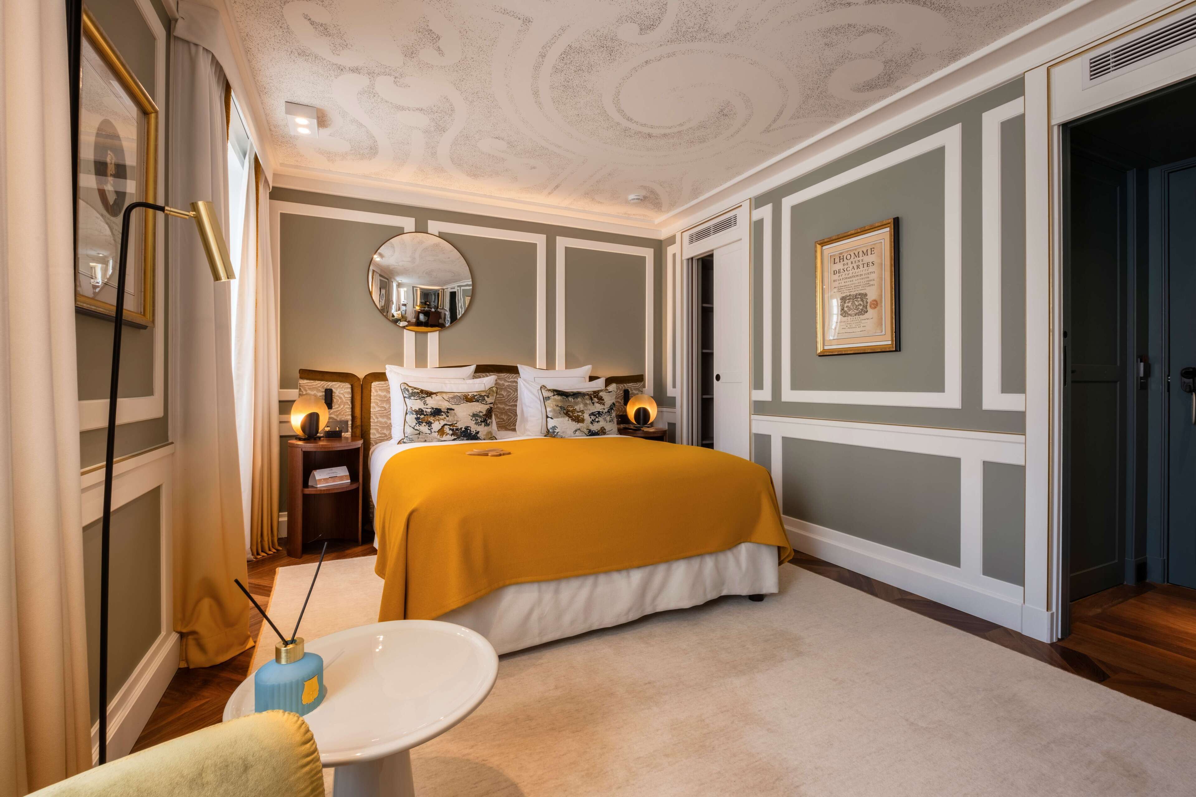 Een slaapkamer met een groot bed, een ronde spiegel, een nachtkastje en een ingelijst certificaat aan de muur.