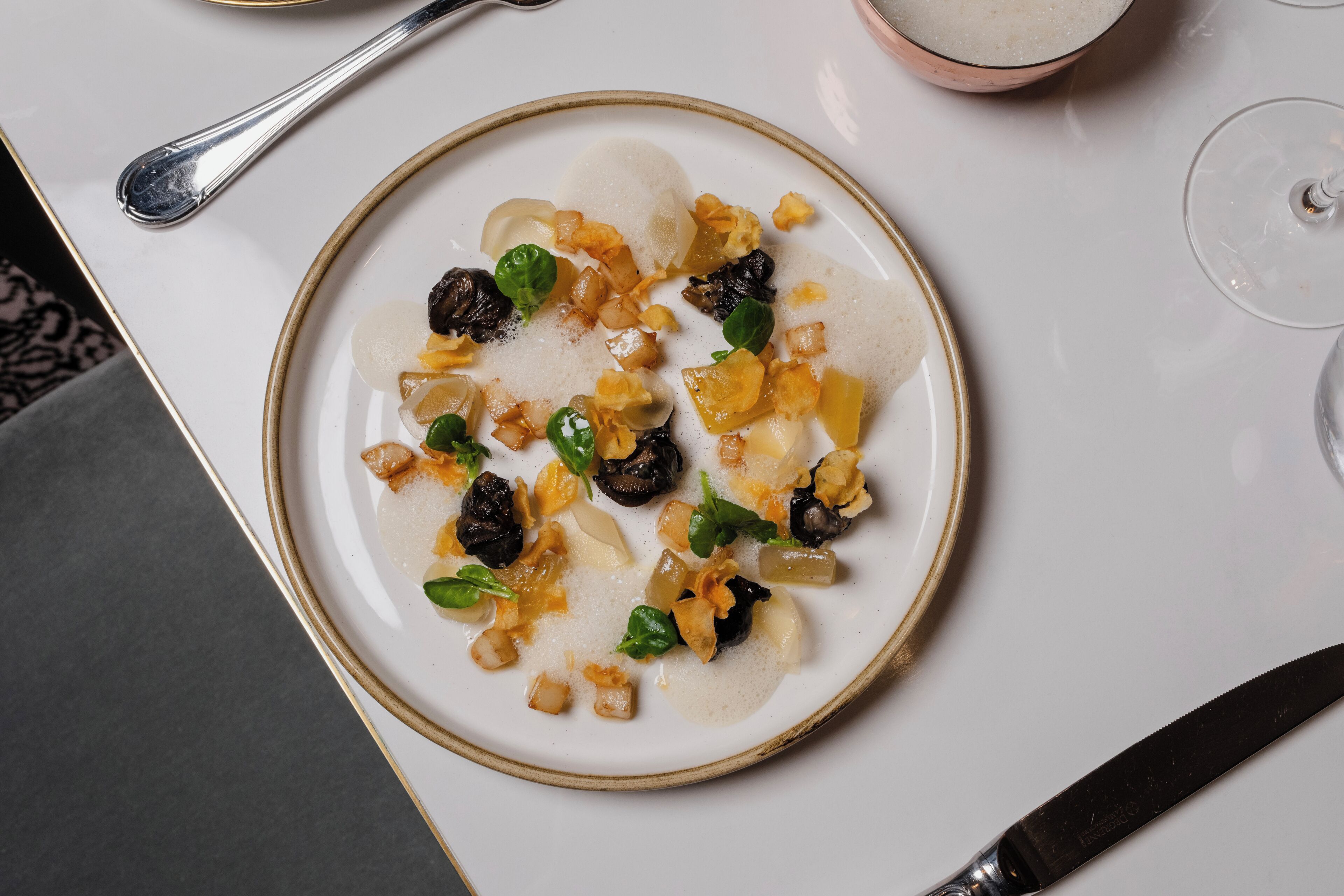 Une assiette remplie de différents aliments, une cuillère et un verre à vin, le tout posé sur une table.