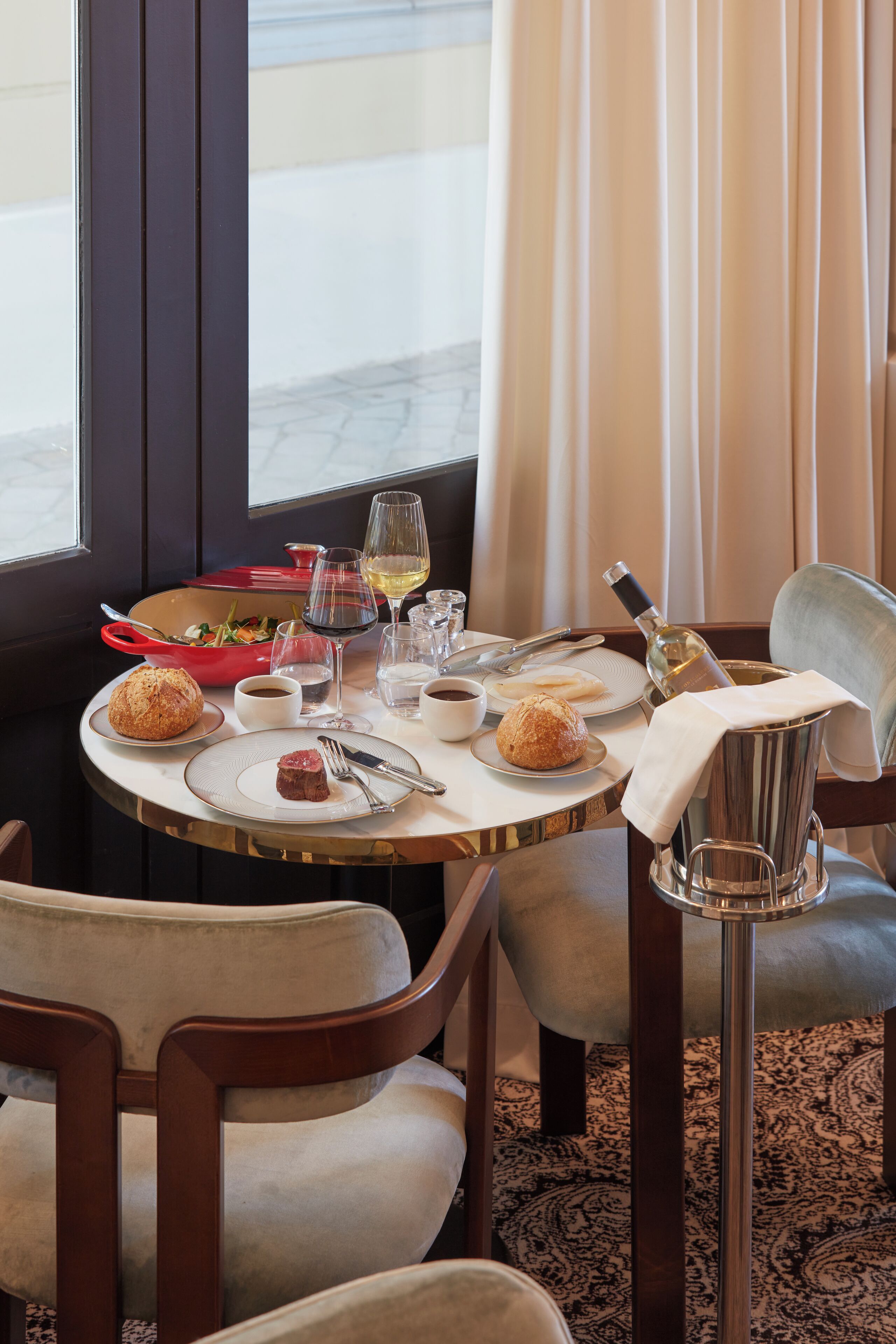 Une table dressée pour le dîner, avec un croissant, une petite assiette de nourriture, un verre de vin et une bouteille d’eau.