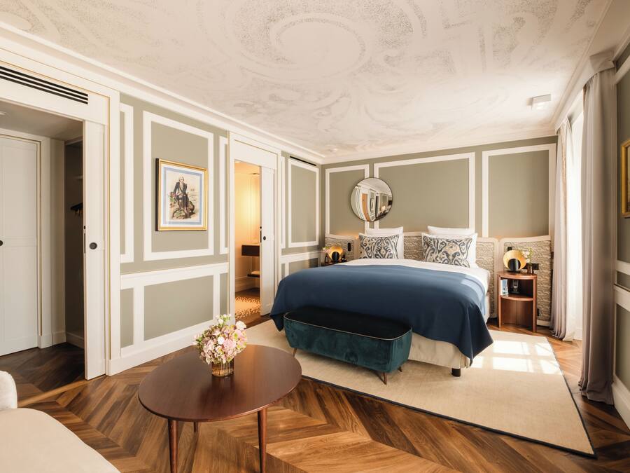 Une chambre à coucher avec un grand lit, une table de chevet, un miroir et une porte donnant sur une autre pièce.