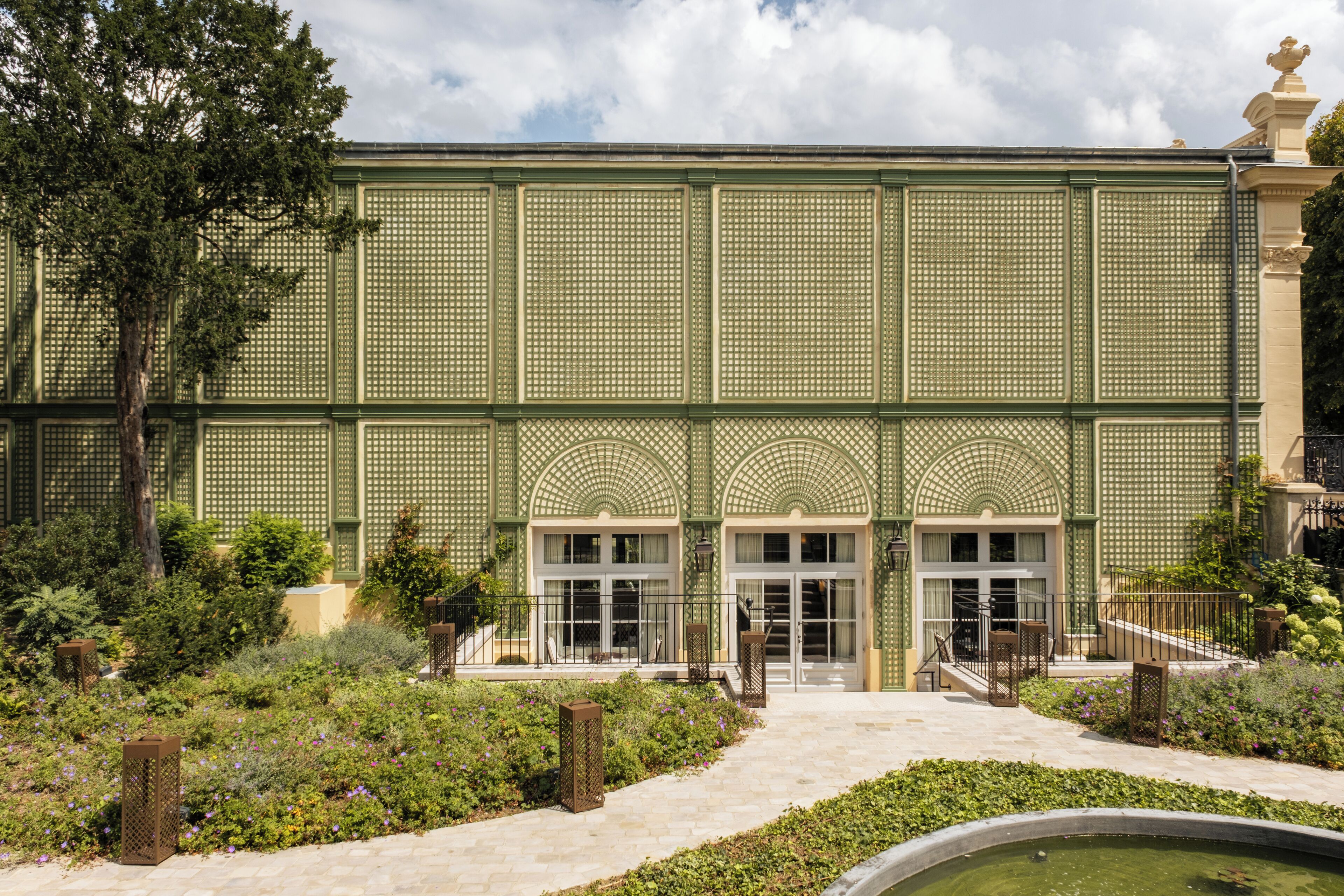 A building with a green lattice facade, large arched windows, and a central entrance with steps.